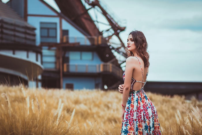 Girl in floral dress in a field with industrial background
