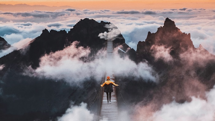 Person on a bridge above clouds and mountains