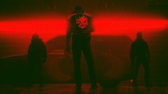 Three figures in front of a car with red lighting