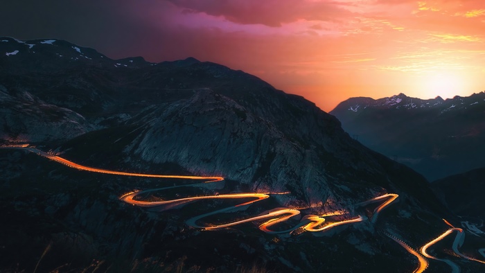 Mountain road with car lights at sunset