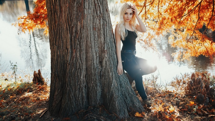 Blonde model in black tank top and jeans by a tree in autumn