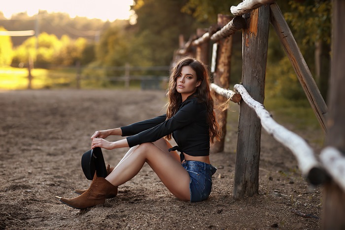 Cowgirl with hat sitting by wooden fence