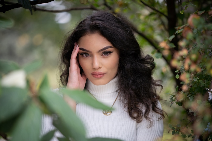 Young woman with dark curly hair wearing a white turtleneck