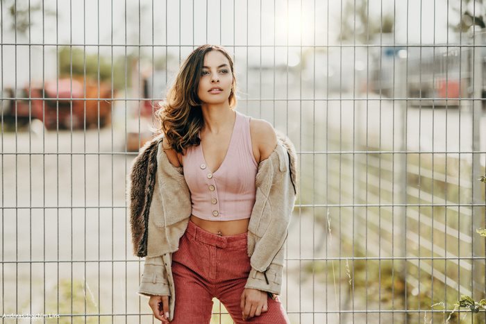 Model in pink top and corduroy pants near fence