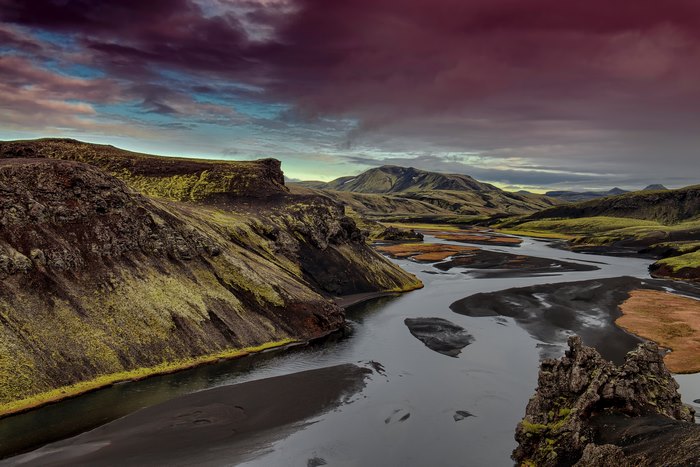 River flowing through mossy mountains under a dramatic sky