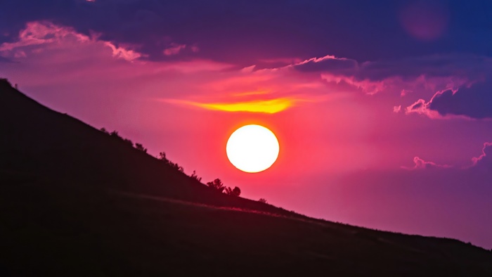 Sunset over a silhouetted hill with colorful clouds