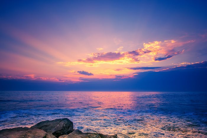Ocean sunset with sun rays and rocks