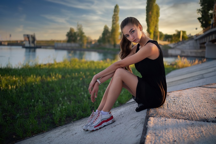 Girl in black dress sitting by river at sunset