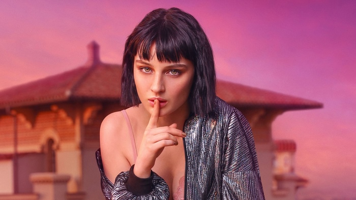 Woman with finger on lips in front of building