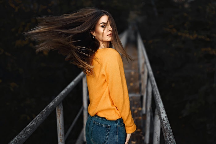 Girl in orange sweater and jeans on a bridge