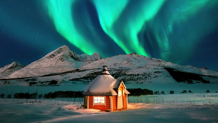 Aurora Borealis over snowy mountains and cabin