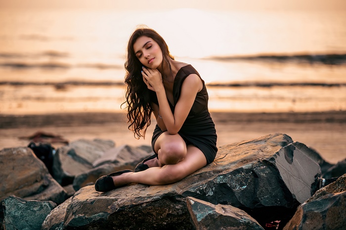 Girl in black dress sitting on rocks at sunset