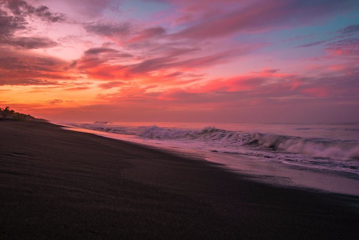 Sunset over a dark sand beach with waves
