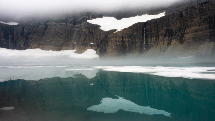 Mountain cliff with snow and lake reflection