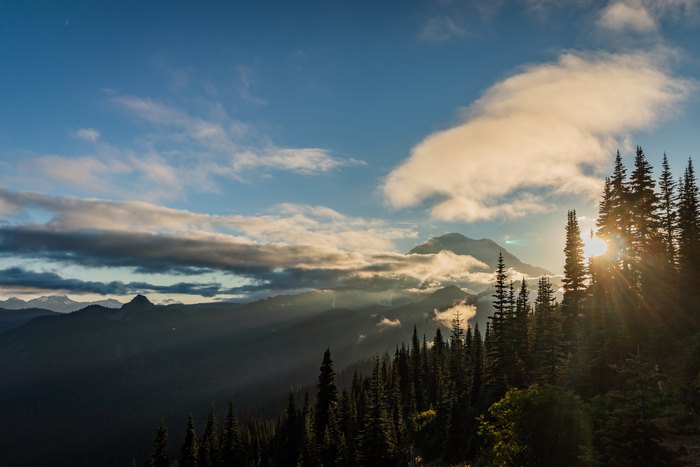 Mountain peak with sunbeams through clouds and trees
