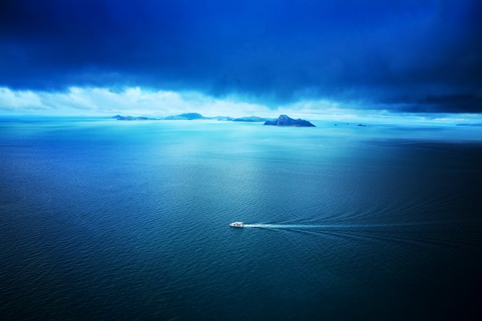 Boat sailing on the ocean towards islands under dark clouds