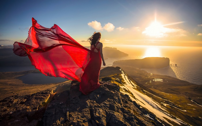 Woman in red dress on mountain peak at sunset