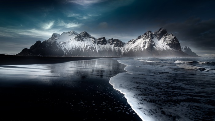 Snow-capped mountains on a black sand beach with ocean waves