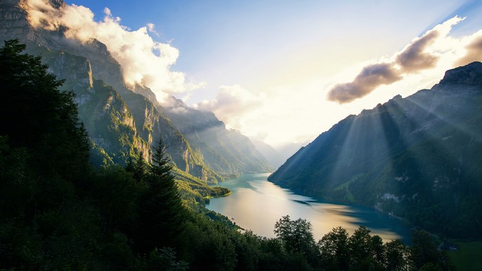 Mountains and lake at sunrise with sunbeams