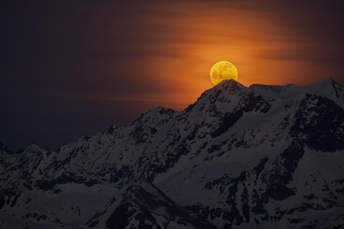 Full moon over snow-covered mountains at dusk