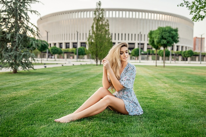 Blonde model sitting on grass in front of stadium