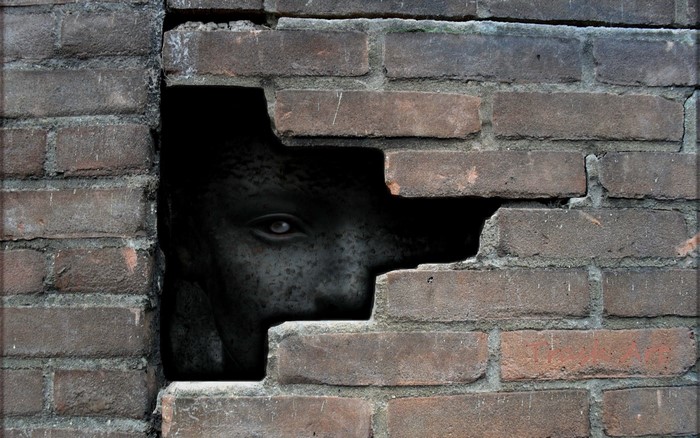Spooky face peeking through a broken brick wall