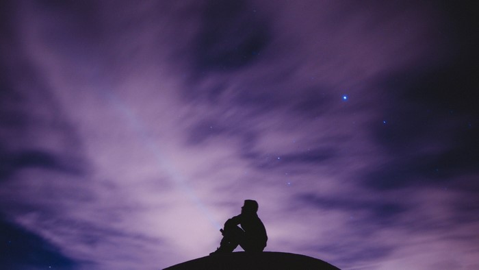 Silhouette of a person sitting under a starry purple sky