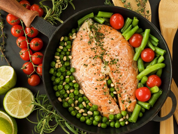 Salmon steak with peas, green beans, and tomatoes in a pan