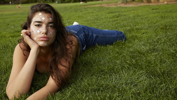 Dua Lipa with glitter makeup lying on grass