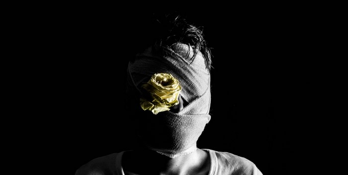 Person with head wrapped in bandages and a yellow rose