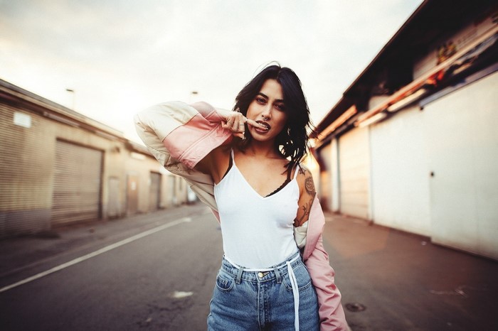 Woman with finger in mouth wearing jacket and jeans