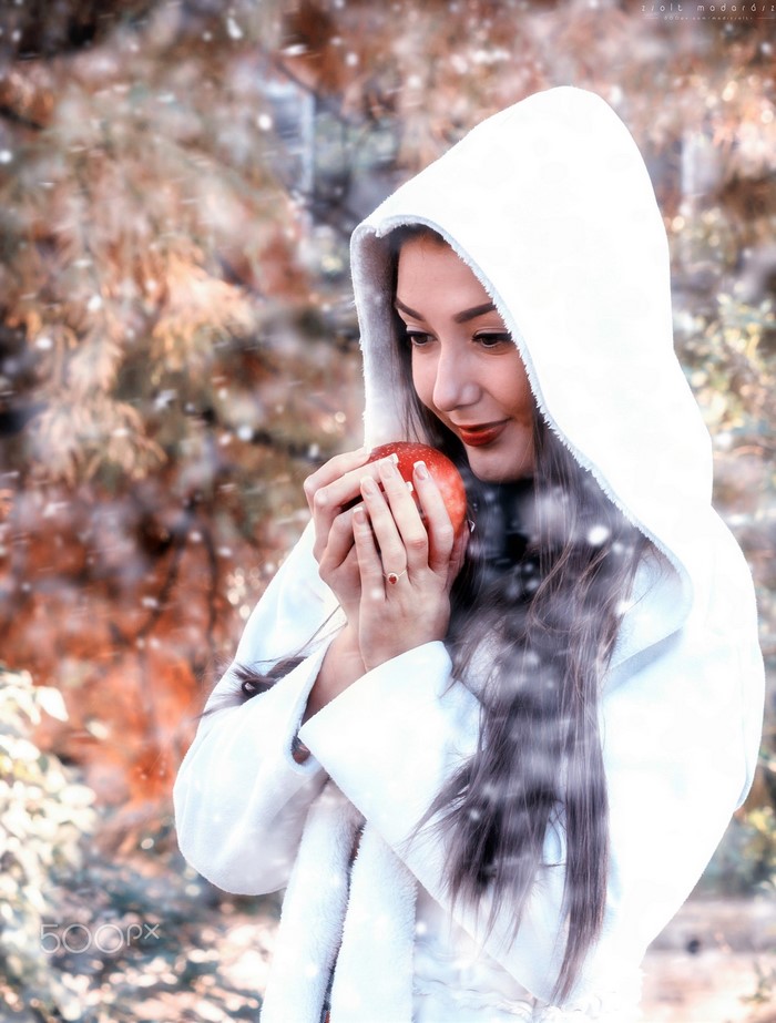 Woman in white coat holding an apple in winter