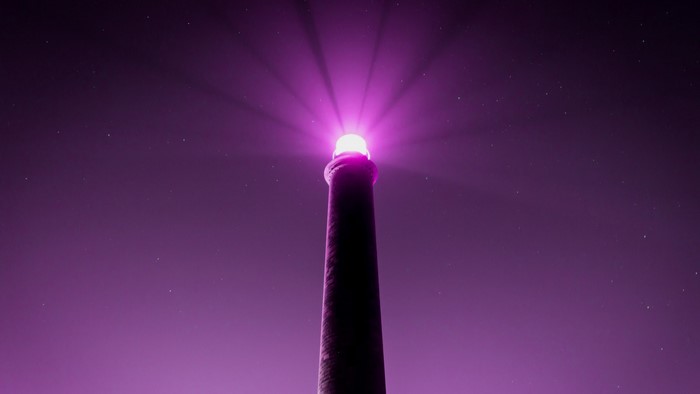 Purple lighthouse beam at night with stars
