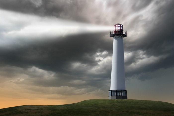 White lighthouse on a grassy hill under stormy clouds