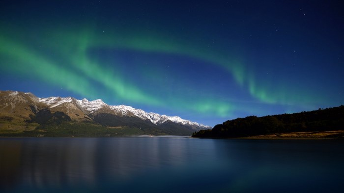 Aurora Borealis over snow-capped mountains and lake