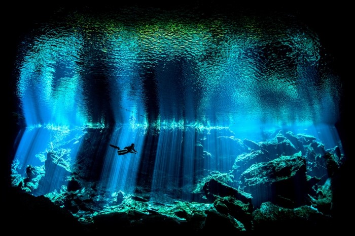 Underwater cave with sun rays and divers