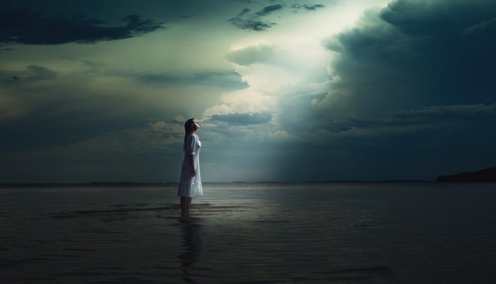 Woman Standing in Ocean Under Dramatic Sky