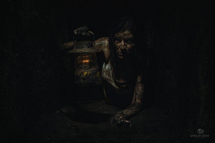 Woman covered in dirt holding a lantern in darkness