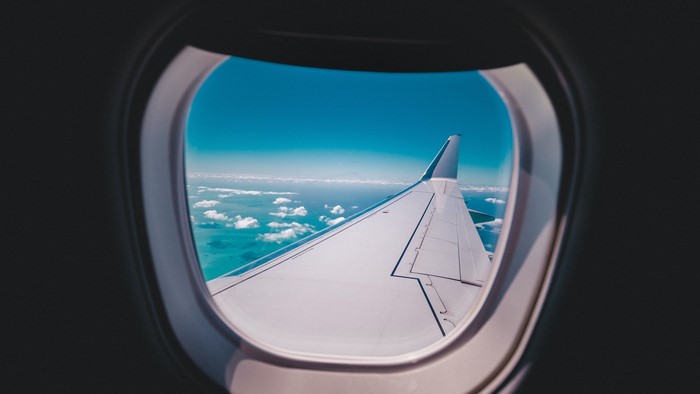 Airplane window view of wing over ocean and clouds