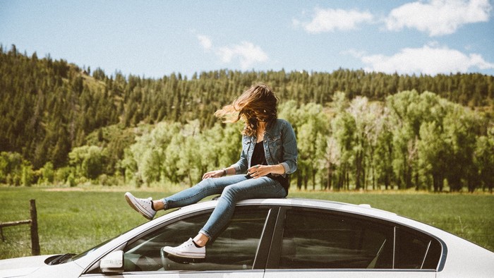 Woman sitting on car roof in a field