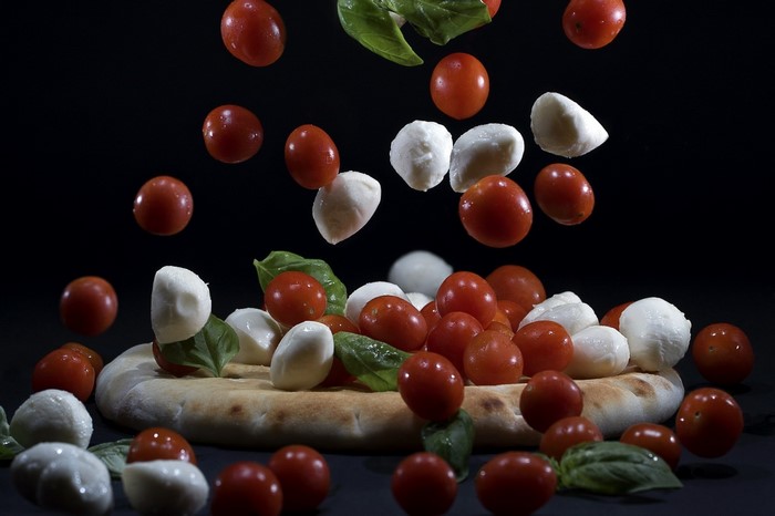 Tomatoes and mozzarella balls falling onto pizza