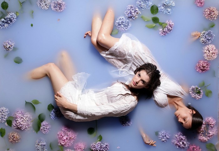 Two women in white dresses floating in water with flowers