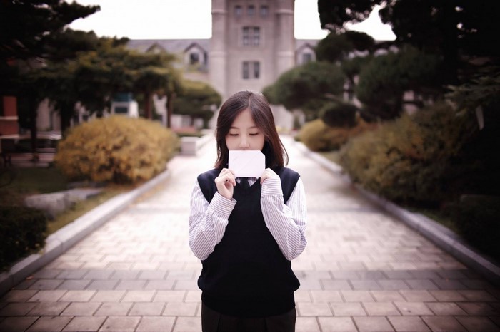 Young woman in school uniform holding a blank card