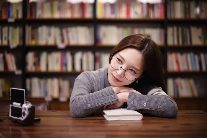 Woman with glasses resting head on book in library