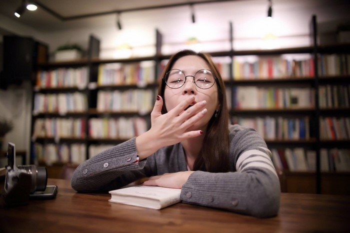Woman yawning in a library with bookshelves