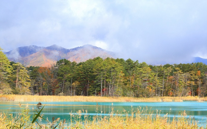 Turquoise lake with autumn trees and misty mountains