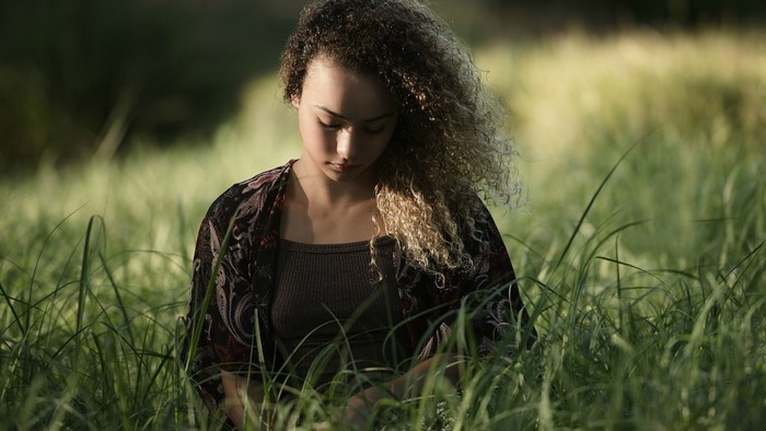 Young woman with curly hair sitting in a grassy field