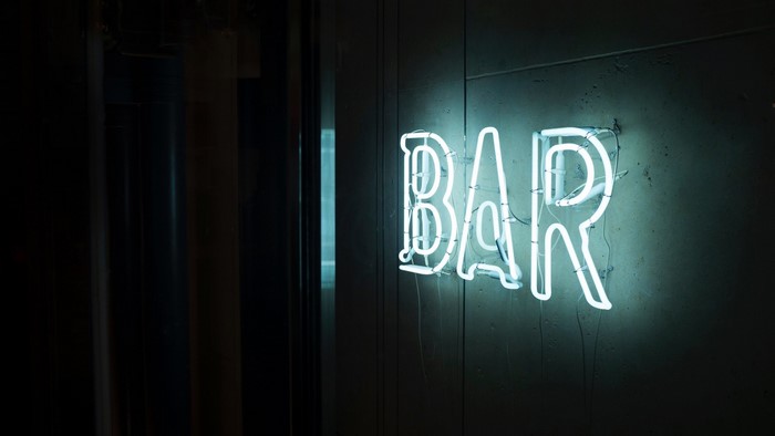 White neon BAR sign on a dark wall