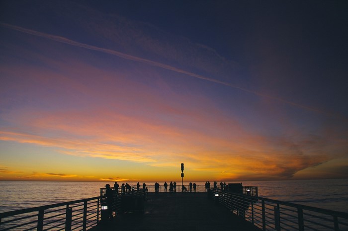 People on a pier watching a sunset over the ocean