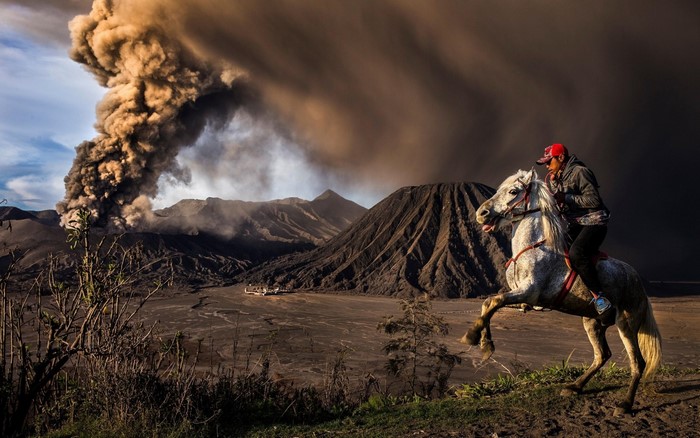 Man riding a horse with a volcano erupting in the background
